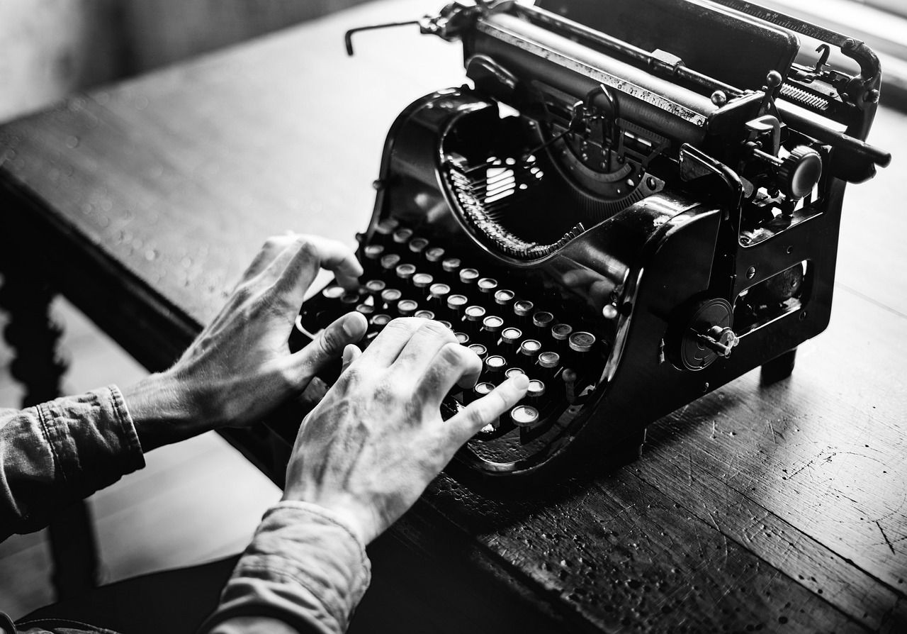 Black and white photo of hands typing on a vintage typewriter on a wooden table.