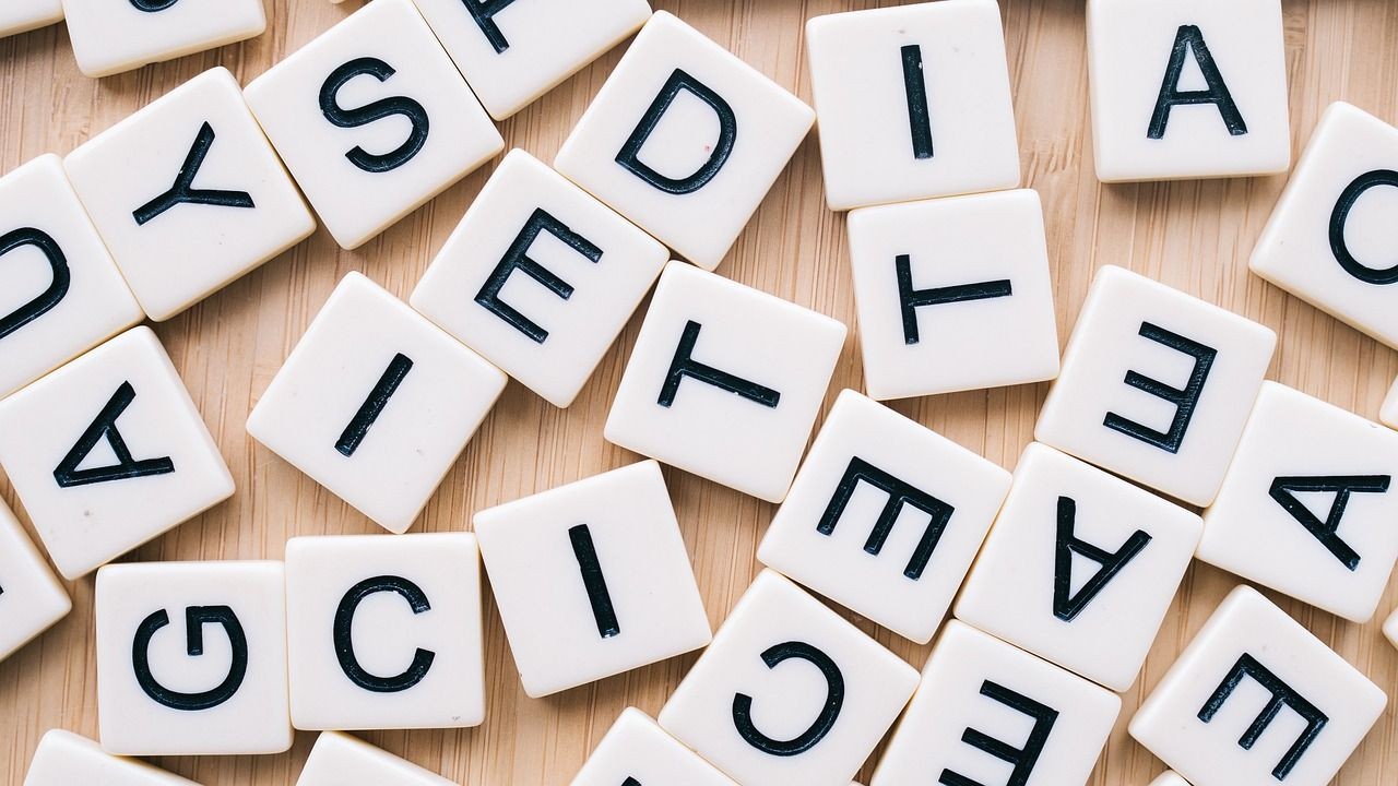 Scattered Scrabble tiles with black letters on a wooden surface.